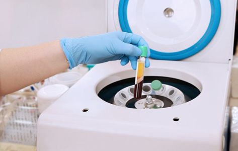 Gloved hand taking vial of blood out of a centrifuge
