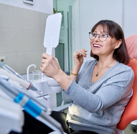 Happy patient looking at her smile in mirror