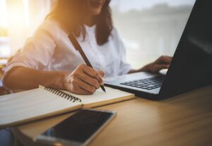 Woman taking notes while researching online